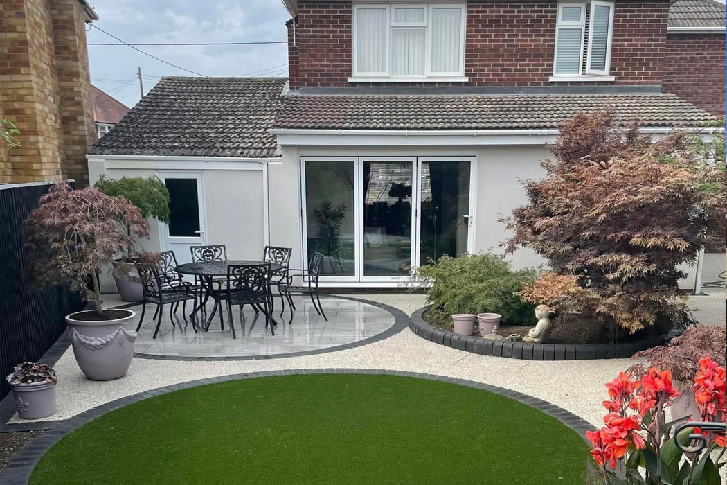 A modern house extension featuring a smooth, off-white spray render finish, overlooking a landscaped garden with a circular artificial lawn and porcelain patio