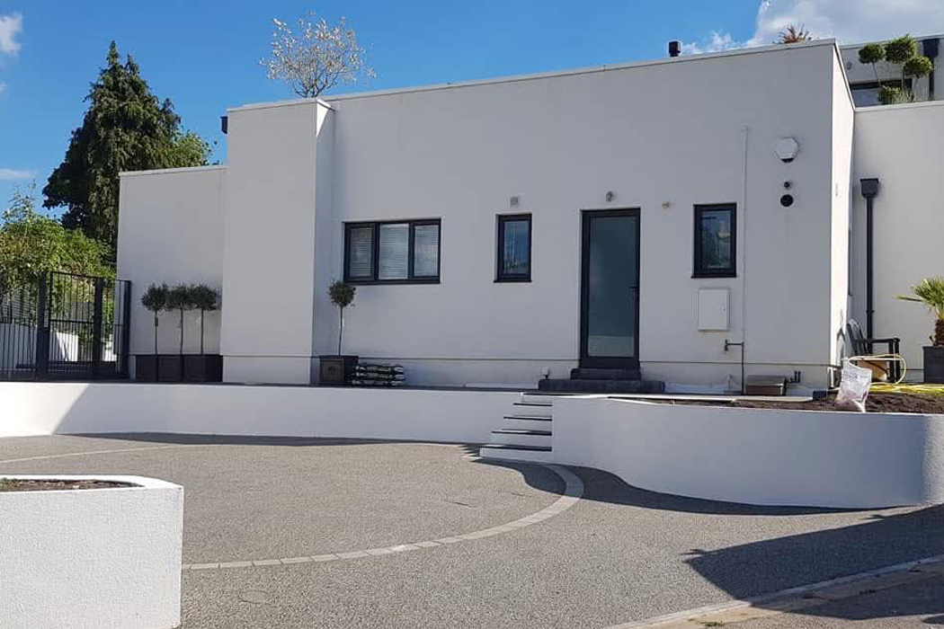 Modern property with high-quality machine-applied spray rendering on exterior walls and a low-level curved retaining wall, demonstrating a smooth, professional finish