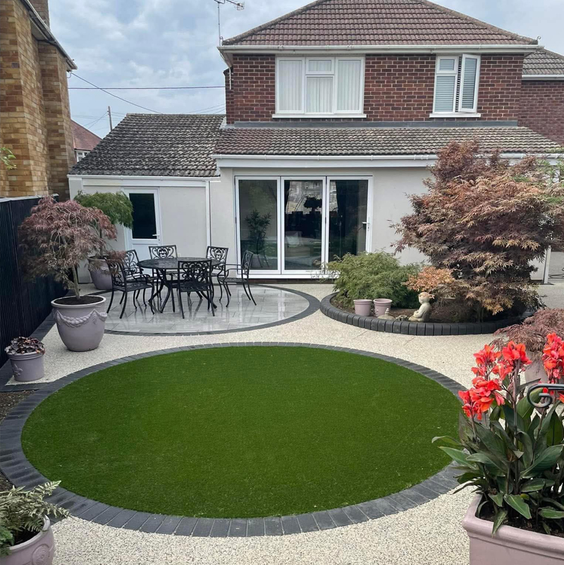 A modern house extension featuring a smooth, off-white spray render finish, overlooking a landscaped garden with a circular artificial lawn and porcelain patio