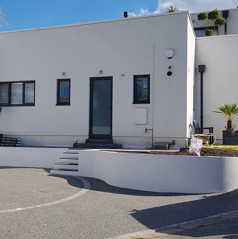 Modern property with high-quality machine-applied spray rendering on exterior walls and a low-level curved retaining wall, demonstrating a smooth, professional finish